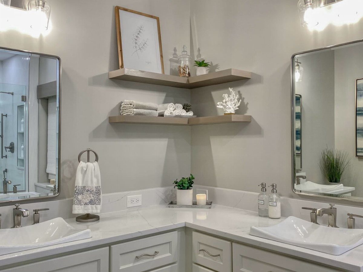 Corner floating wooden shelves styled with plants, white decor, and towels above a marble bathroom vanity.