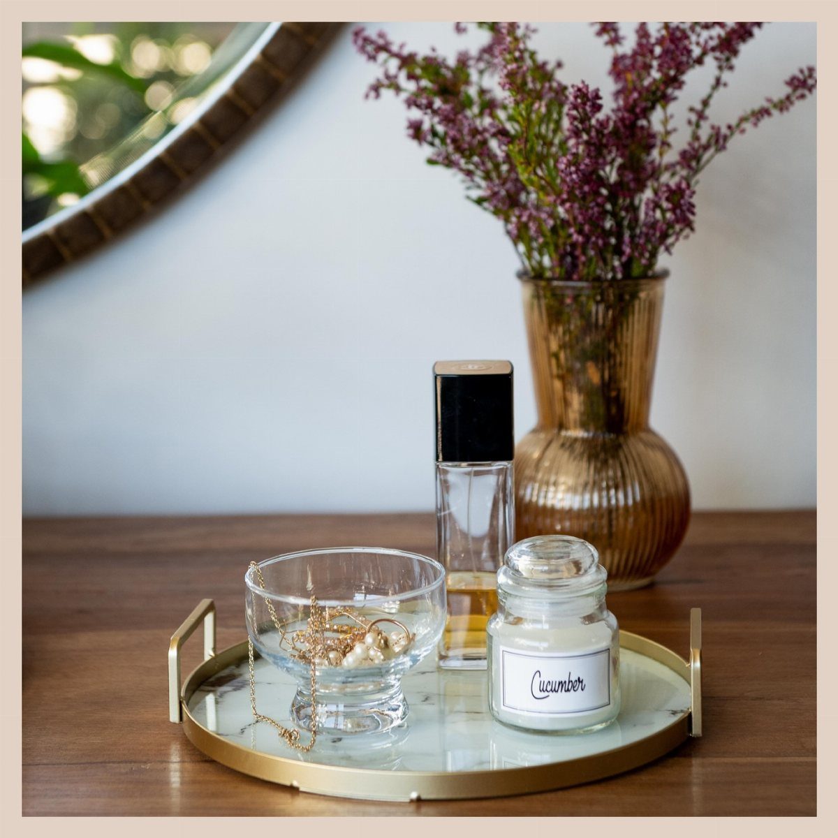 A marble and gold tray holding jewelry, perfume, and a small jar on a wooden table.