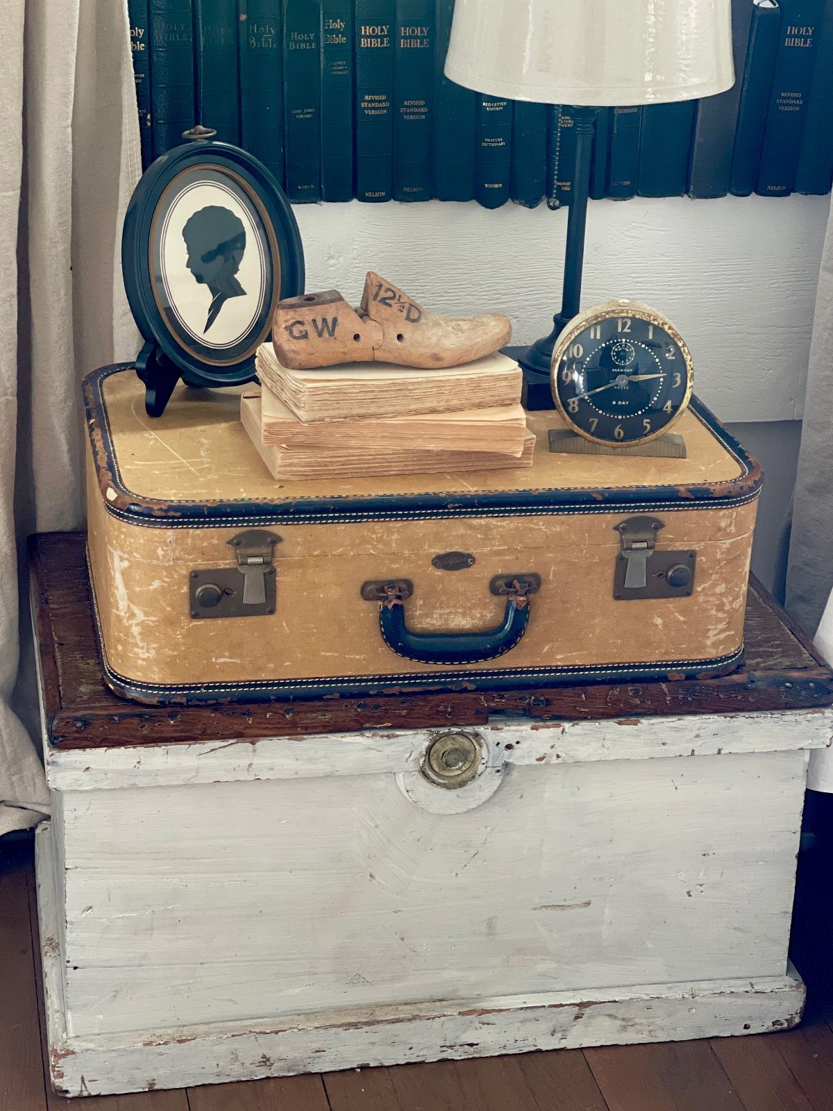 A vintage tan suitcase decorated with a clock and portrait sits on a white chest.
