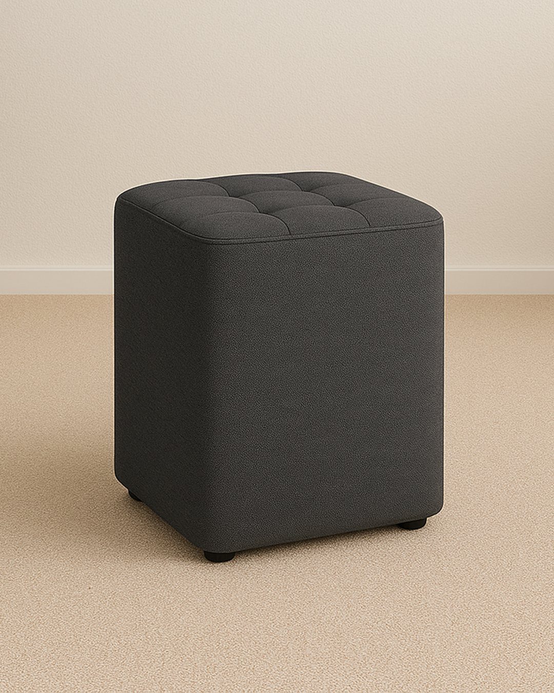 A dark grey tufted square storage ottoman placed on a light beige carpeted floor.