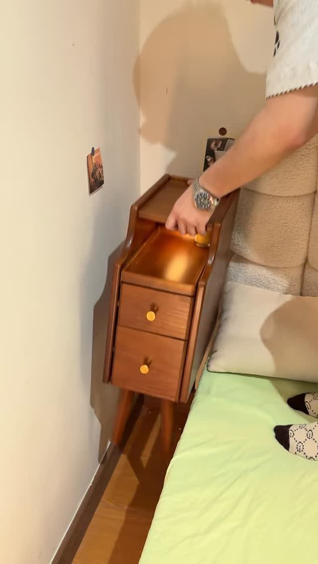 A person reaching for a wooden nightstand with built-in tabletop compartments and drawers.
