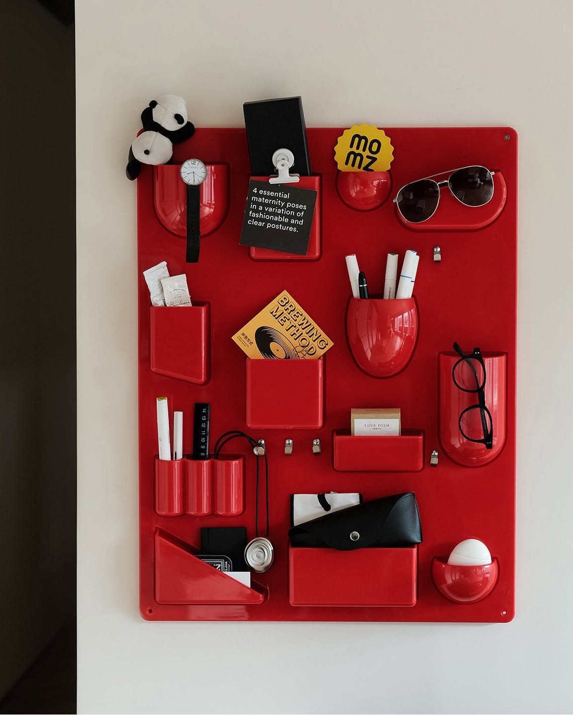 Red wall pocket organizer holding sunglasses, pens, glasses, and various small personal items.
