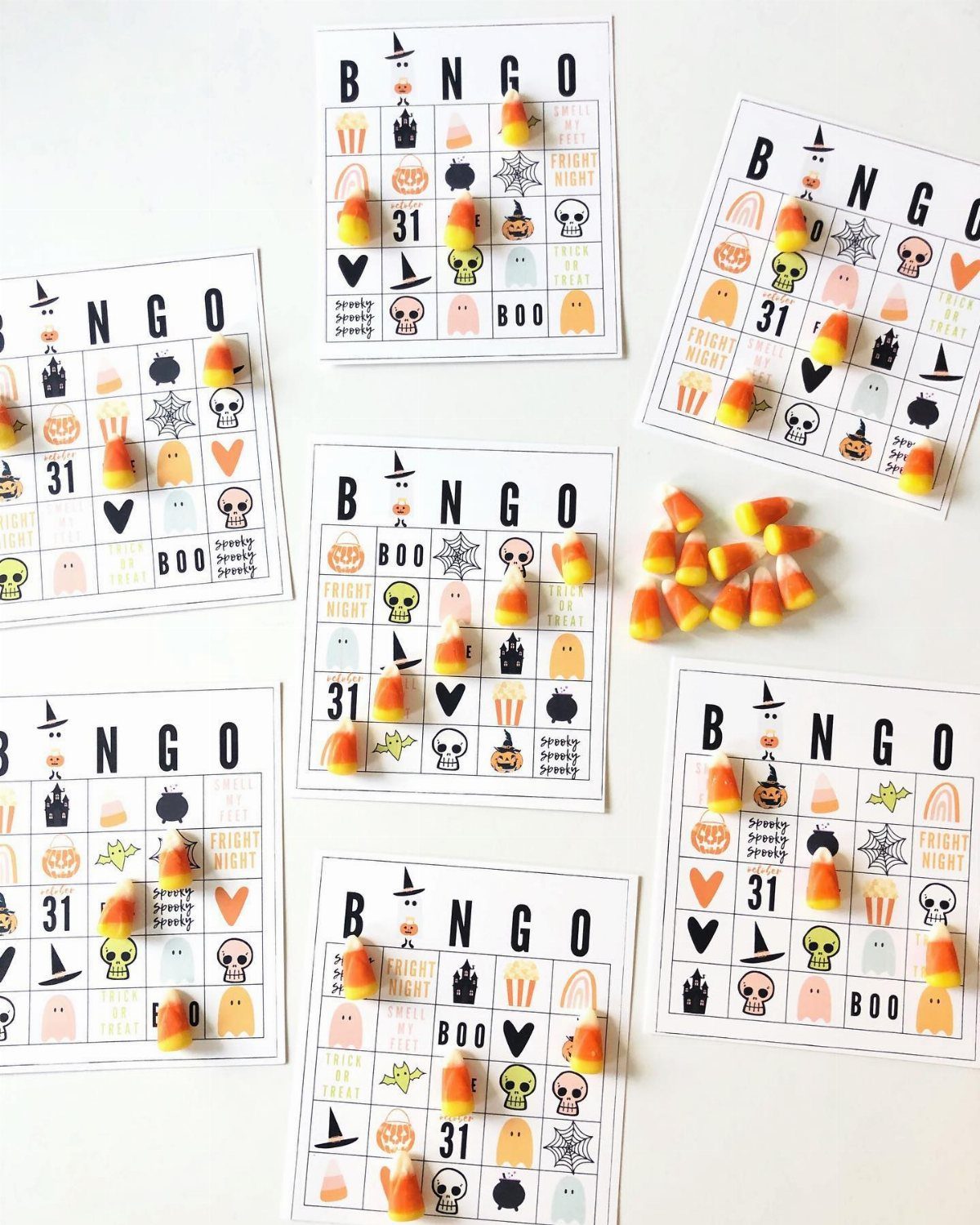 Candy corn pieces placed on various Halloween-themed bingo cards on a white background.