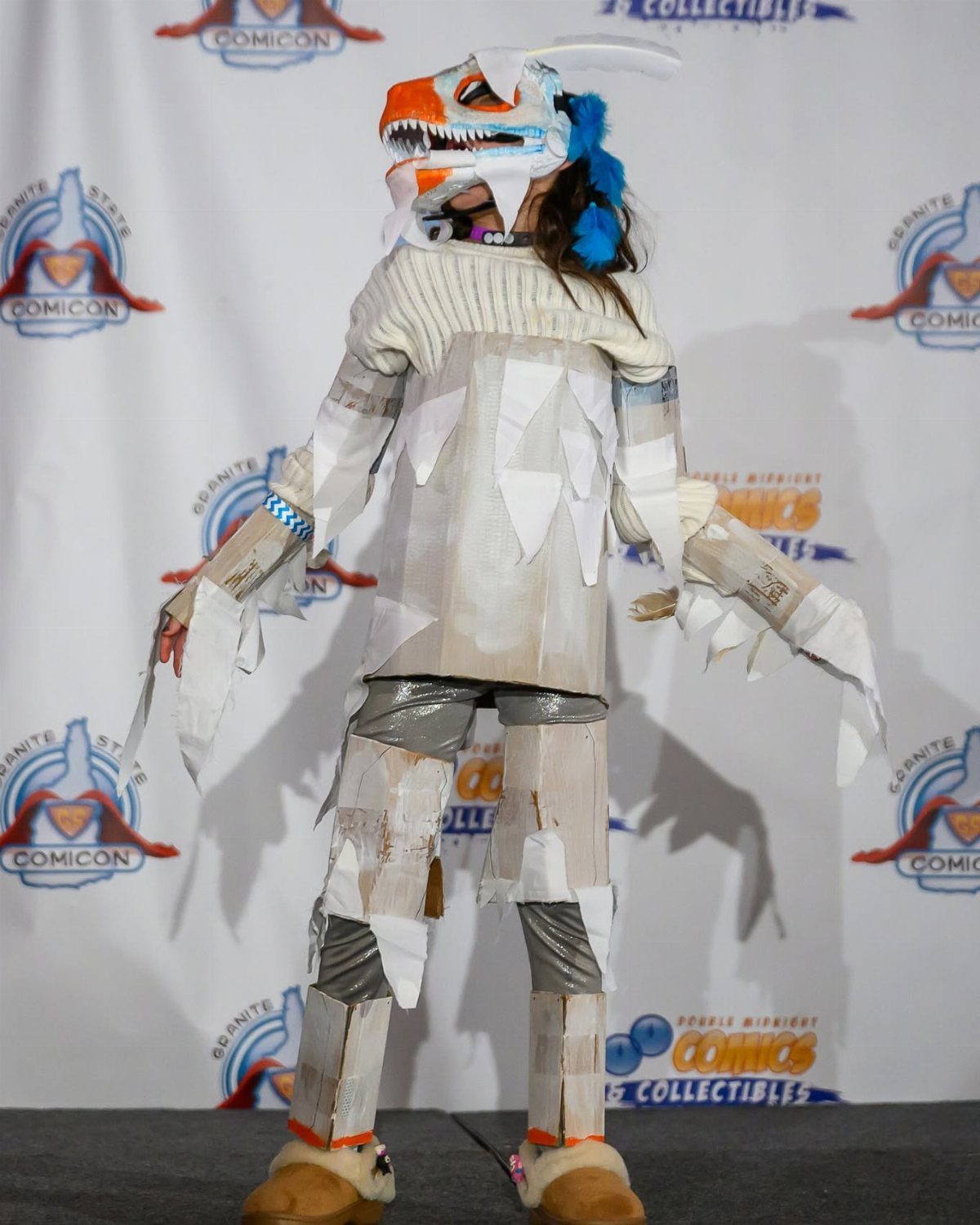 A person wearing a large, handmade white and orange dragon costume standing against a branded backdrop.