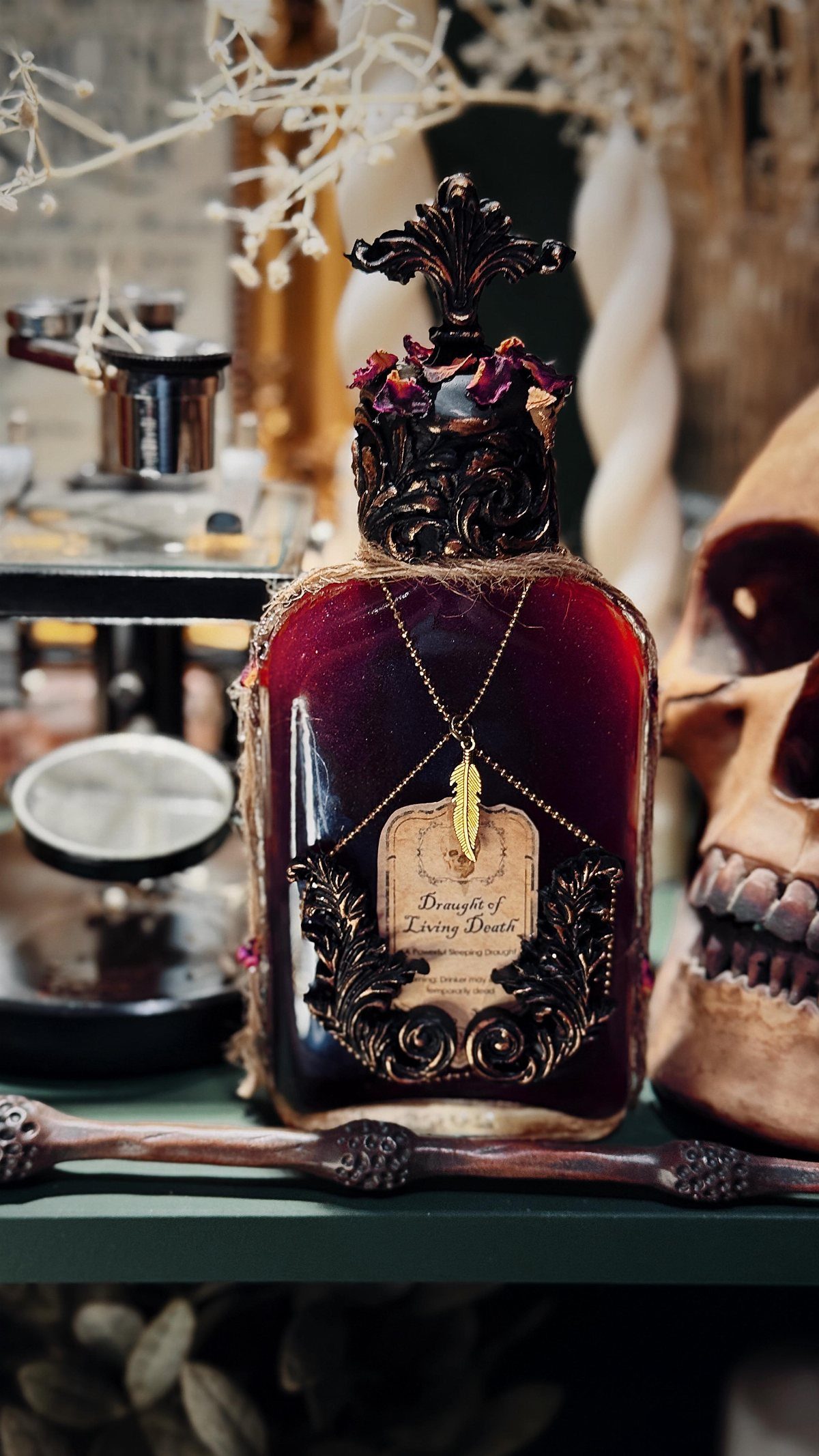 An ornate glass bottle filled with red liquid sits among skulls and candles.