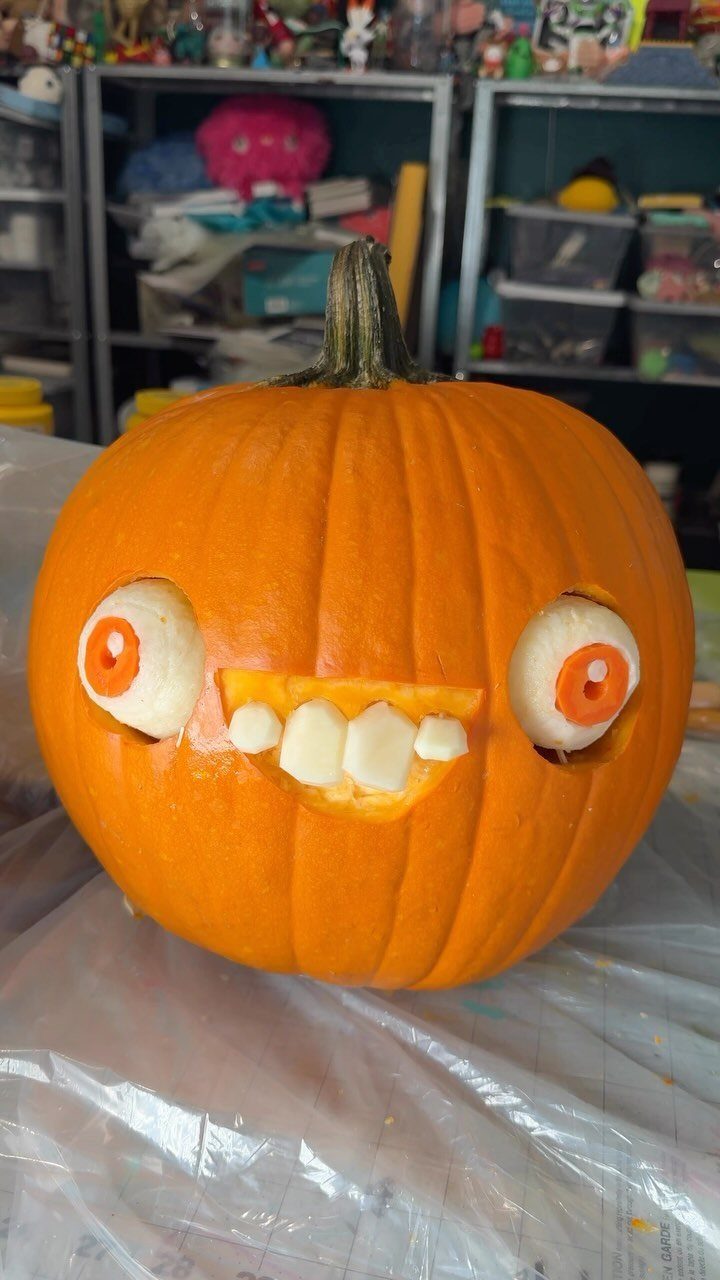 Carved orange pumpkin with large white eyes and a toothy grin on plastic.