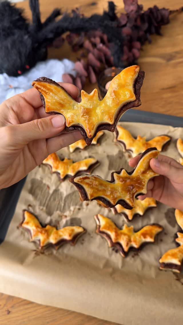 Hands holding bat-shaped Halloween cookies over a baking sheet with more cookies.