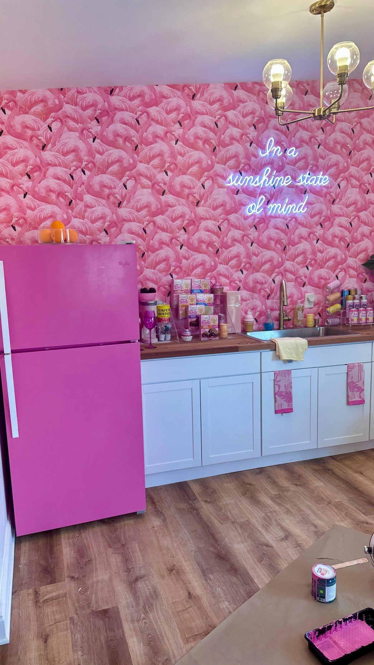 A bright pink painted refrigerator in a kitchen with pink flamingo patterned wallpaper.