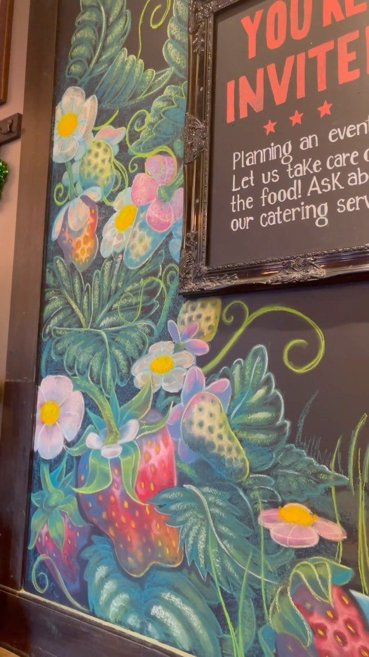 Colorful chalk drawings of strawberries and flowers on a black chalkboard surface.