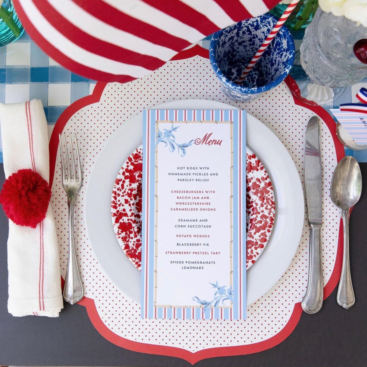 A patriotic table setting with a menu, patterned plates, silverware, and a blue patterned cup.