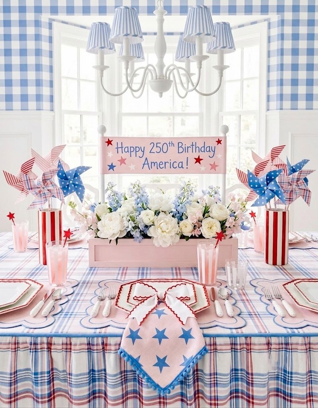 A festive table setting with a plaid tablecloth, floral centerpiece, and patriotic pinwheels.