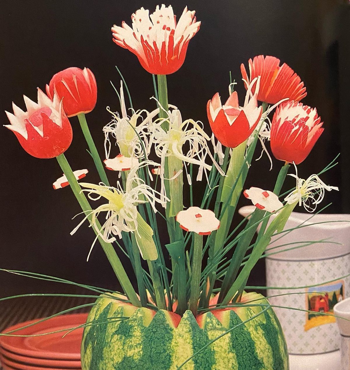 Red and white paper flowers arranged inside a carved watermelon vase.