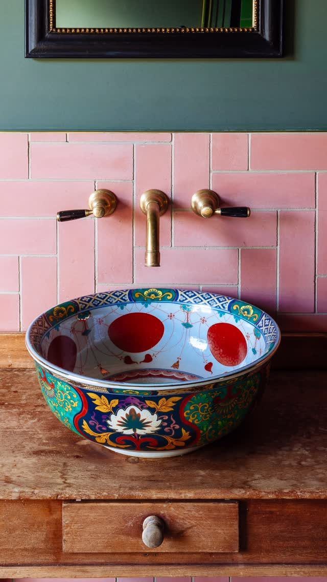 A patterned ceramic sink sits on a wooden vanity against pink tiles and a green wall.