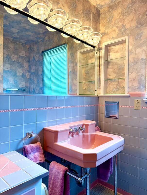 Pink sink with chrome fixtures set against light blue tiled walls in a bathroom.
