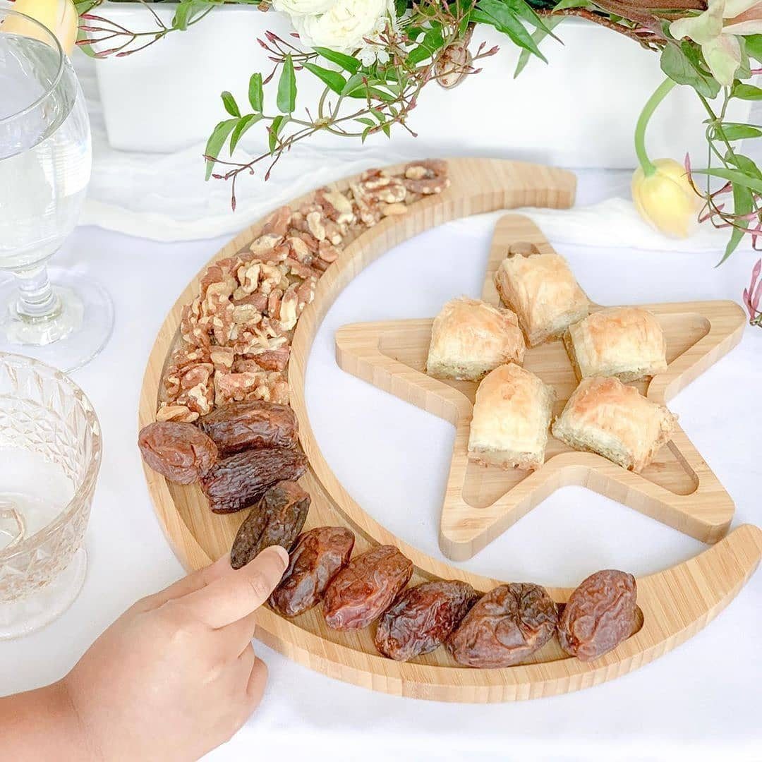 Wooden crescent moon and star shaped trays filled with dates, nuts, and baklava on a table.