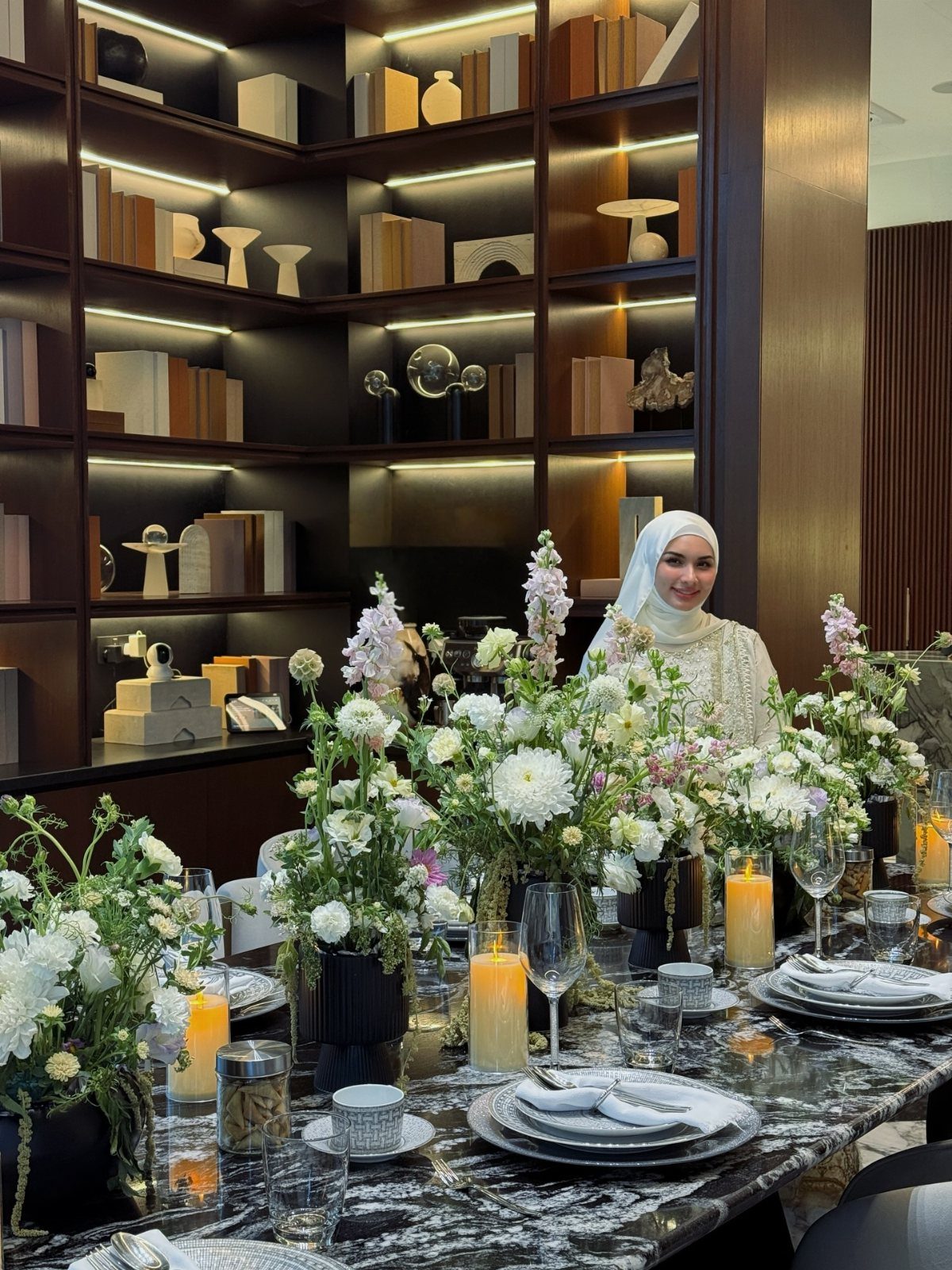 Elegant table setting with white floral centerpieces, lit candles, and marble tabletop in a modern room.