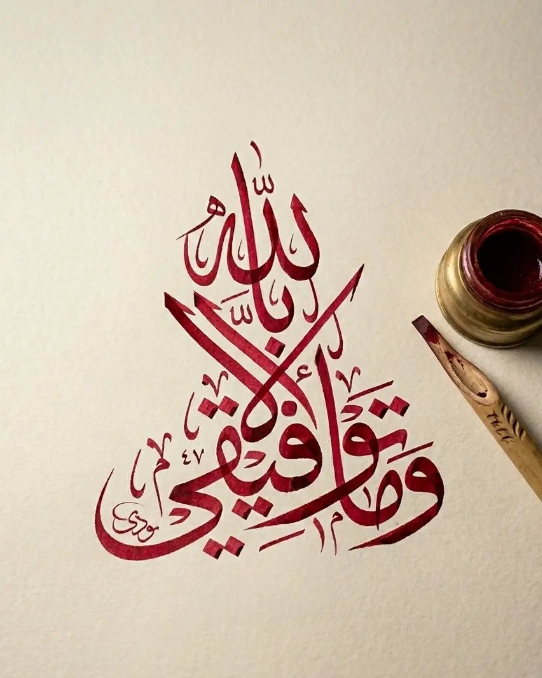 Red Arabic calligraphy art on cream paper with a brass inkwell and wooden pen.