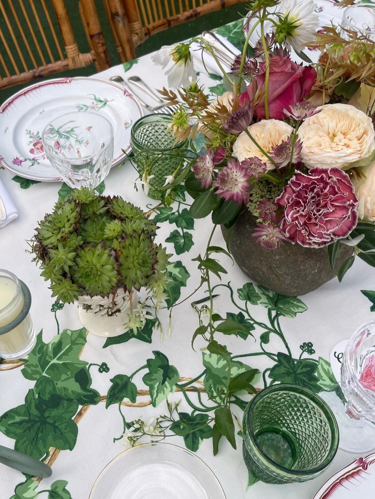 Floral arrangement in a stone vase with ivy vines on a decorated white tablecloth.