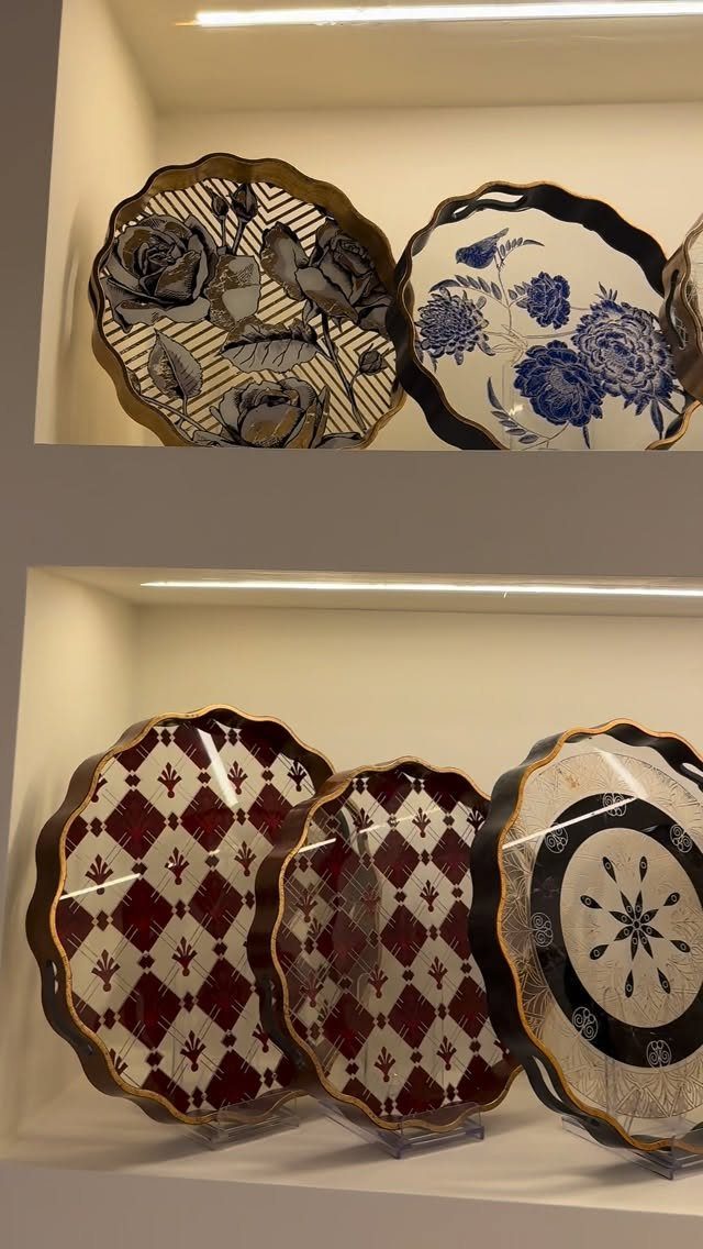 Decorative scalloped trays with floral and geometric patterns displayed on white recessed shelves.