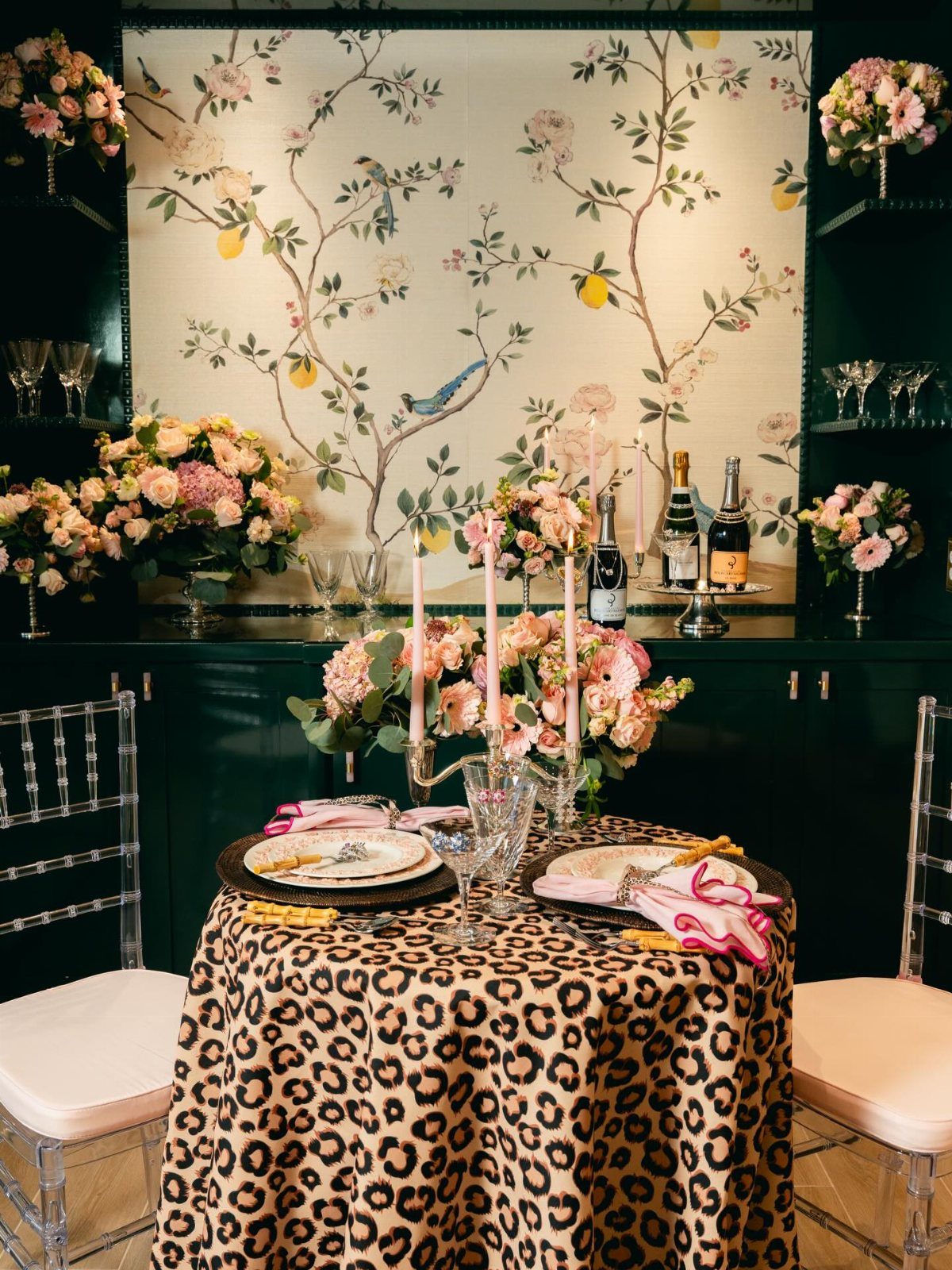 A dining table with leopard print cloth, pink roses, and taper candles set for a formal meal.