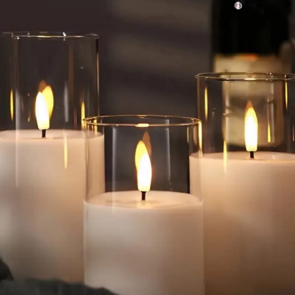 Three white LED pillar candles with glowing flames inside gold-rimmed glass cylinders.