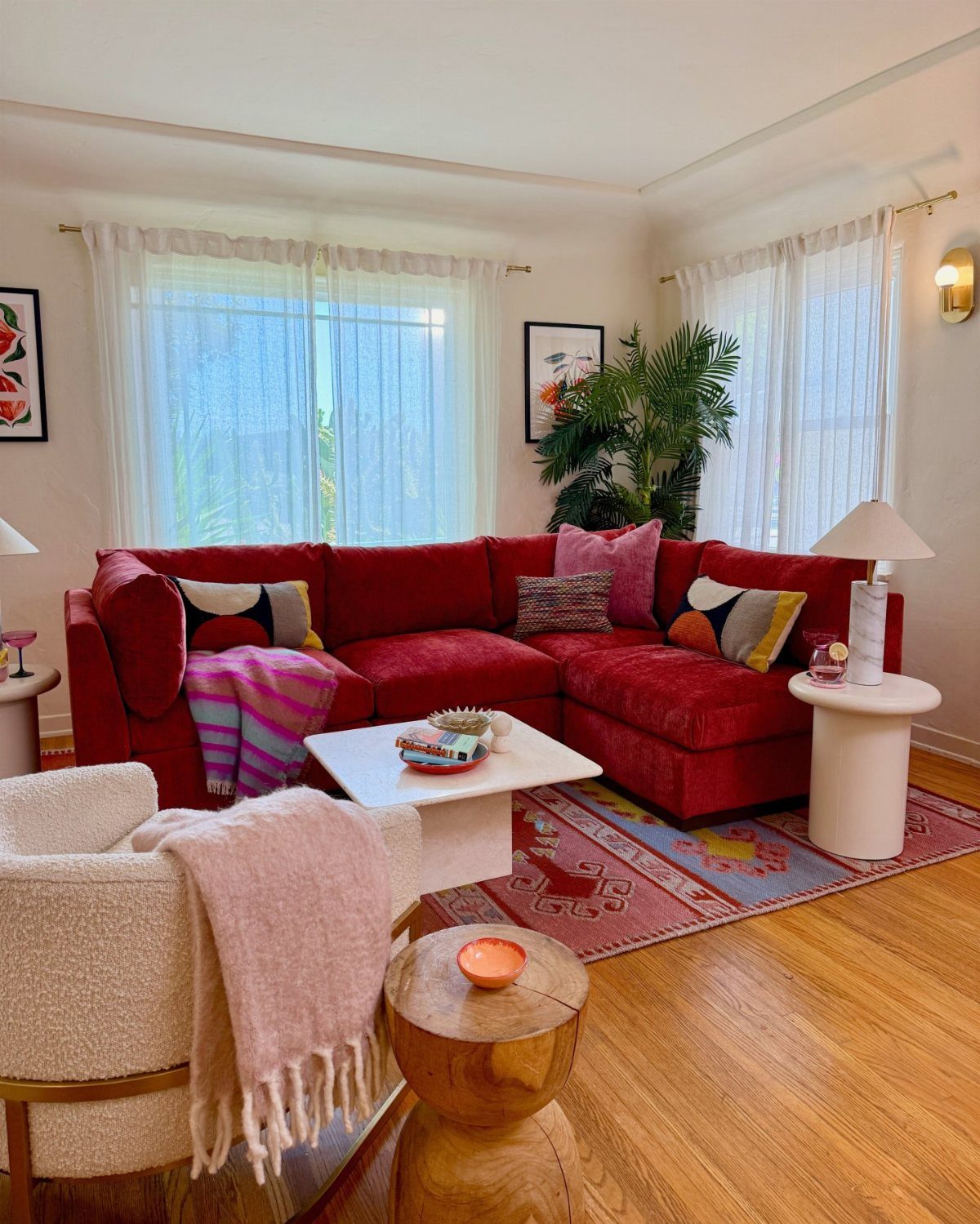 A large muted red sectional sofa surrounded by cozy textures and bright windows.
