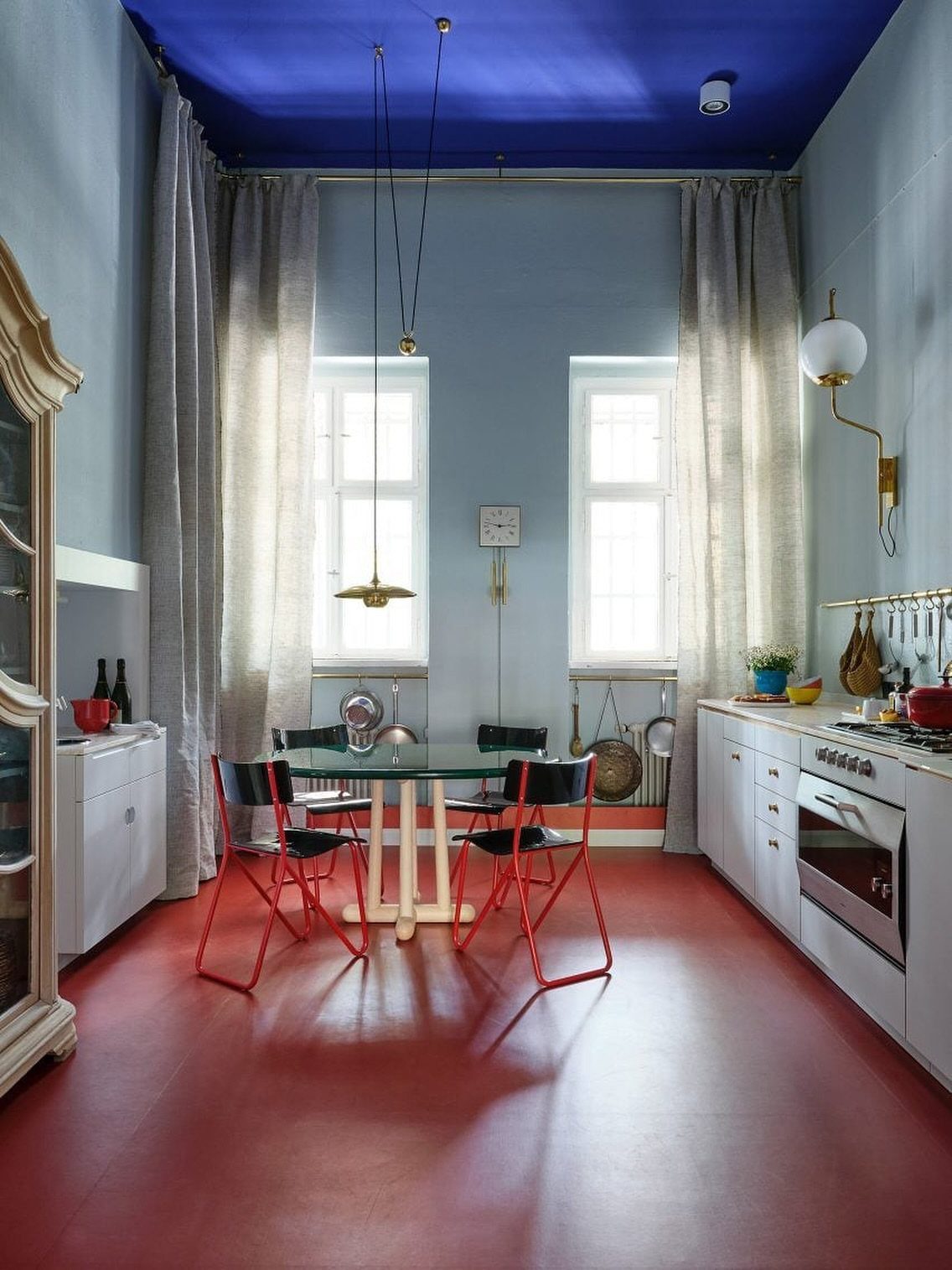 Red floor in a dining room with blue ceiling, light blue walls, and a glass table.