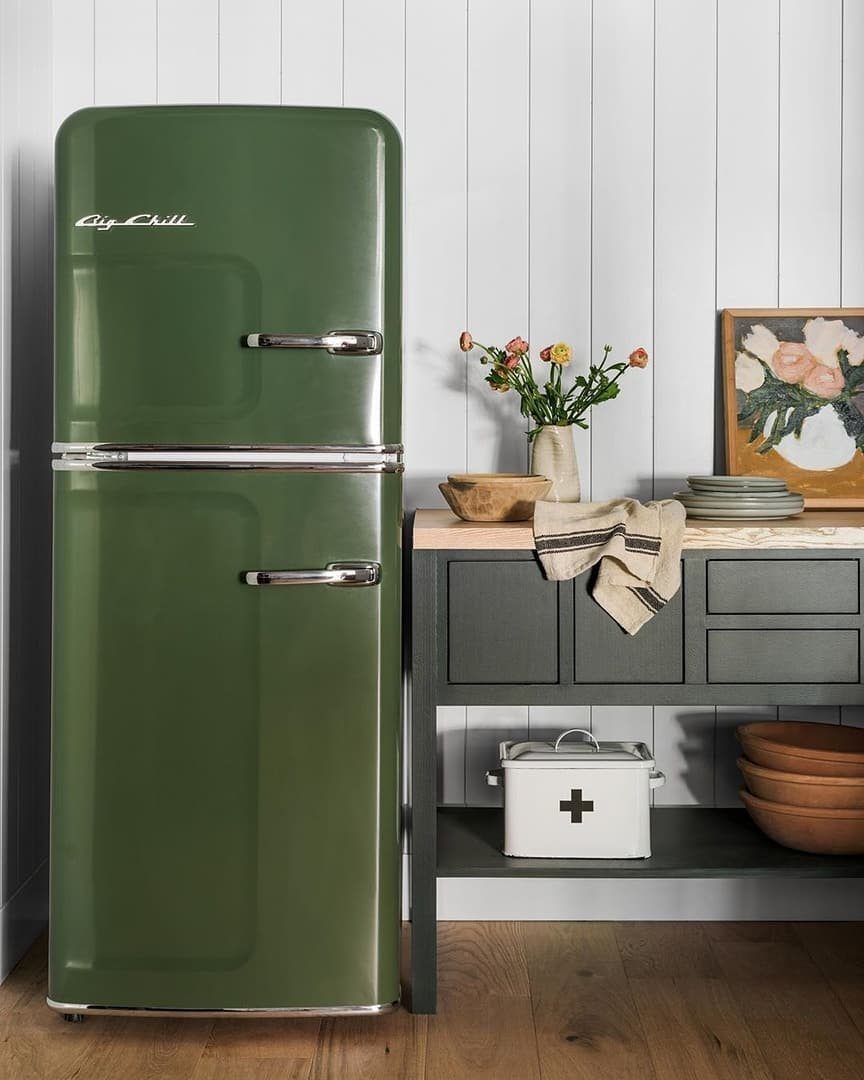 Olive green retro refrigerator standing next to a dark grey sideboard in a white paneled room.
