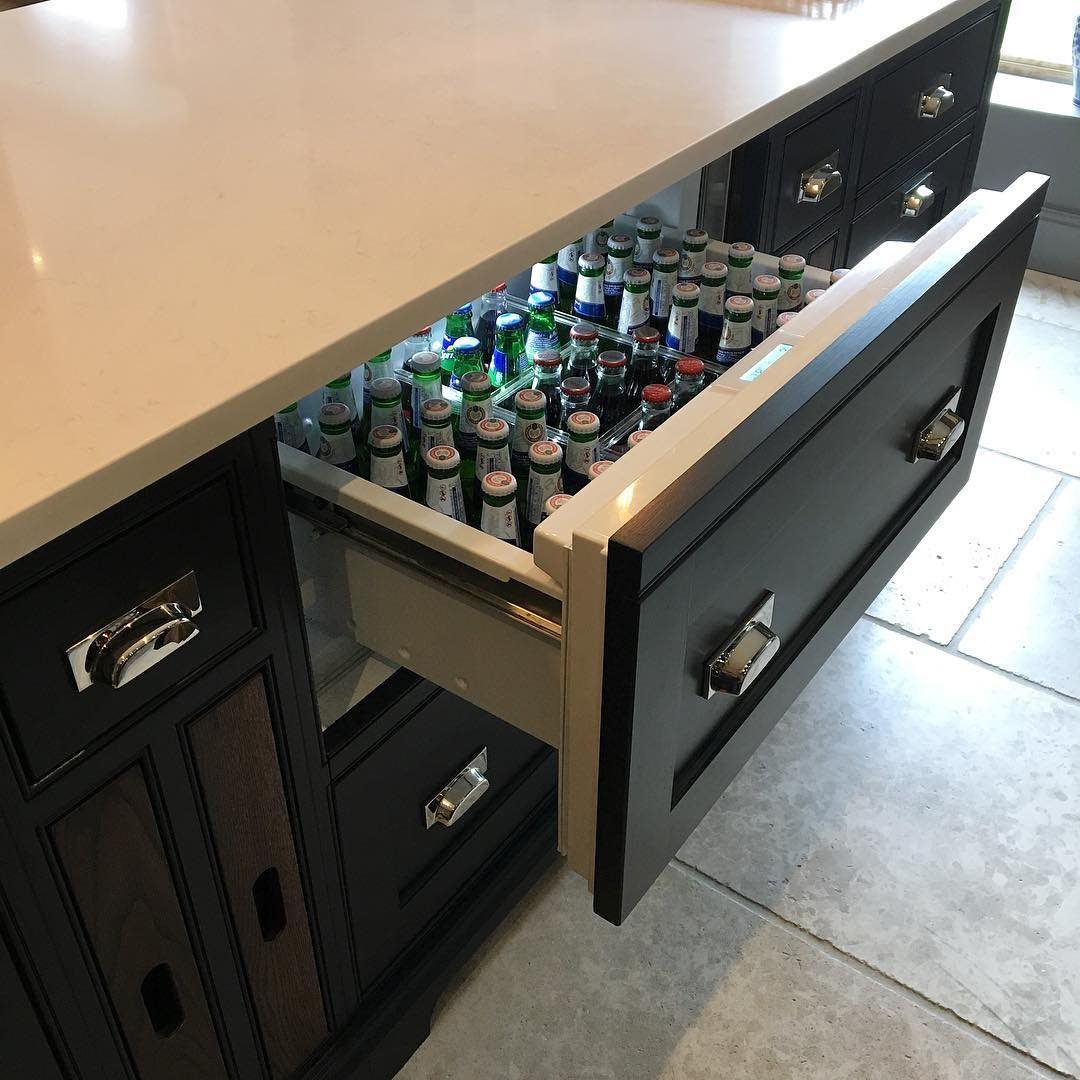 An open undercounter refrigerator drawer filled with glass beverage bottles inside a dark kitchen island.