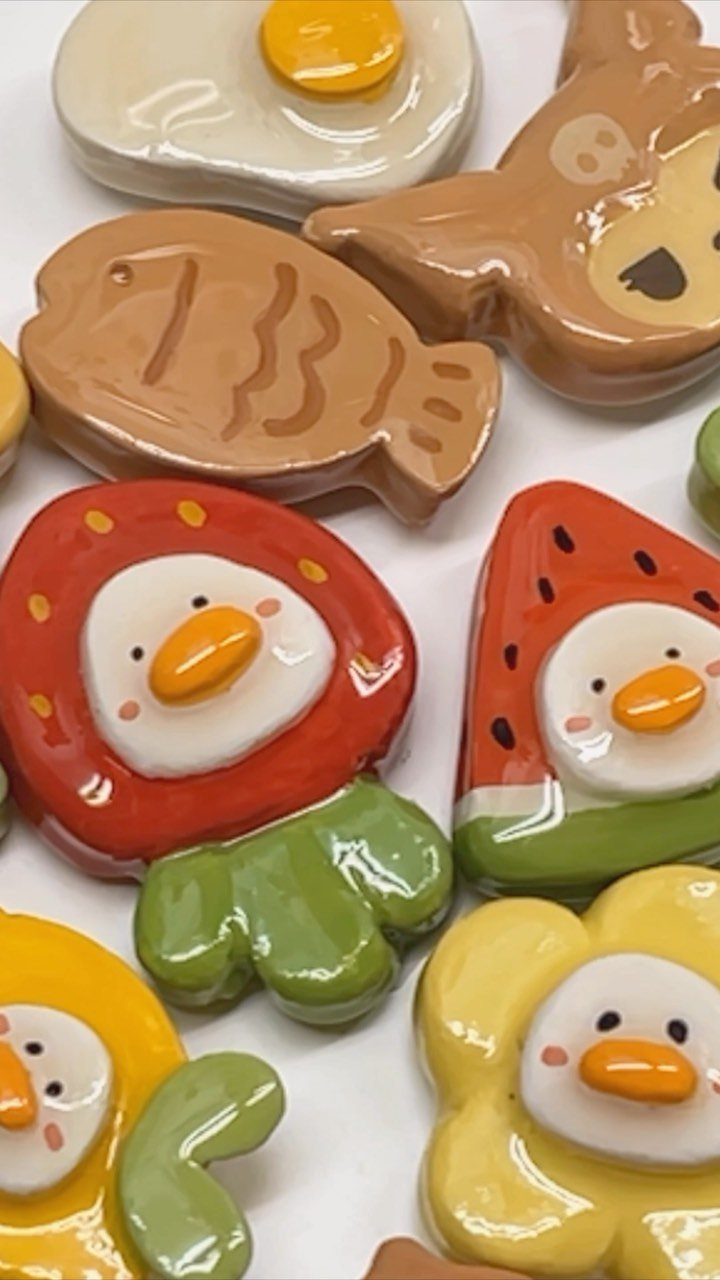 Colorful shaped clay magnets including a fish, strawberry, and fried egg on a white background.