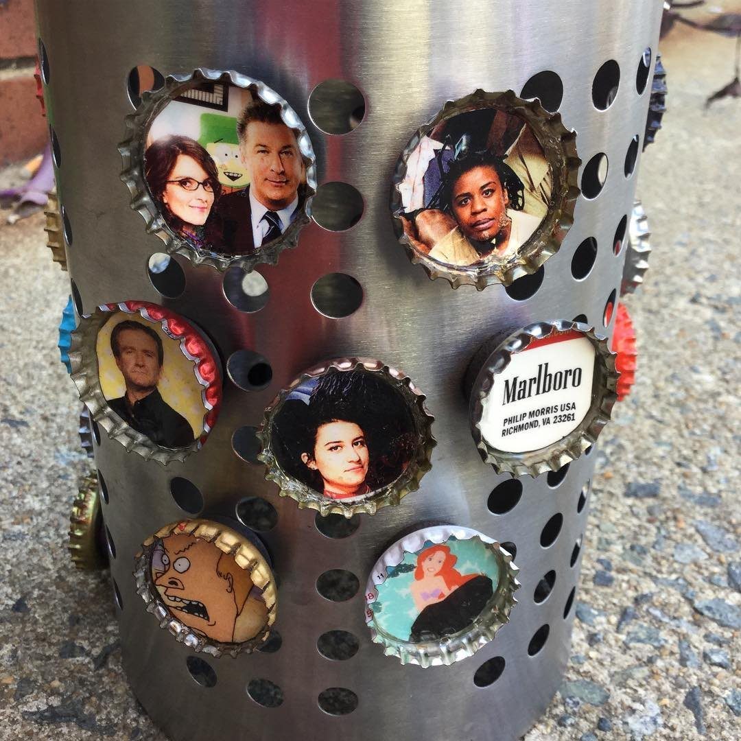 Bottle cap magnets with various printed faces and logos attached to a metal cylinder.