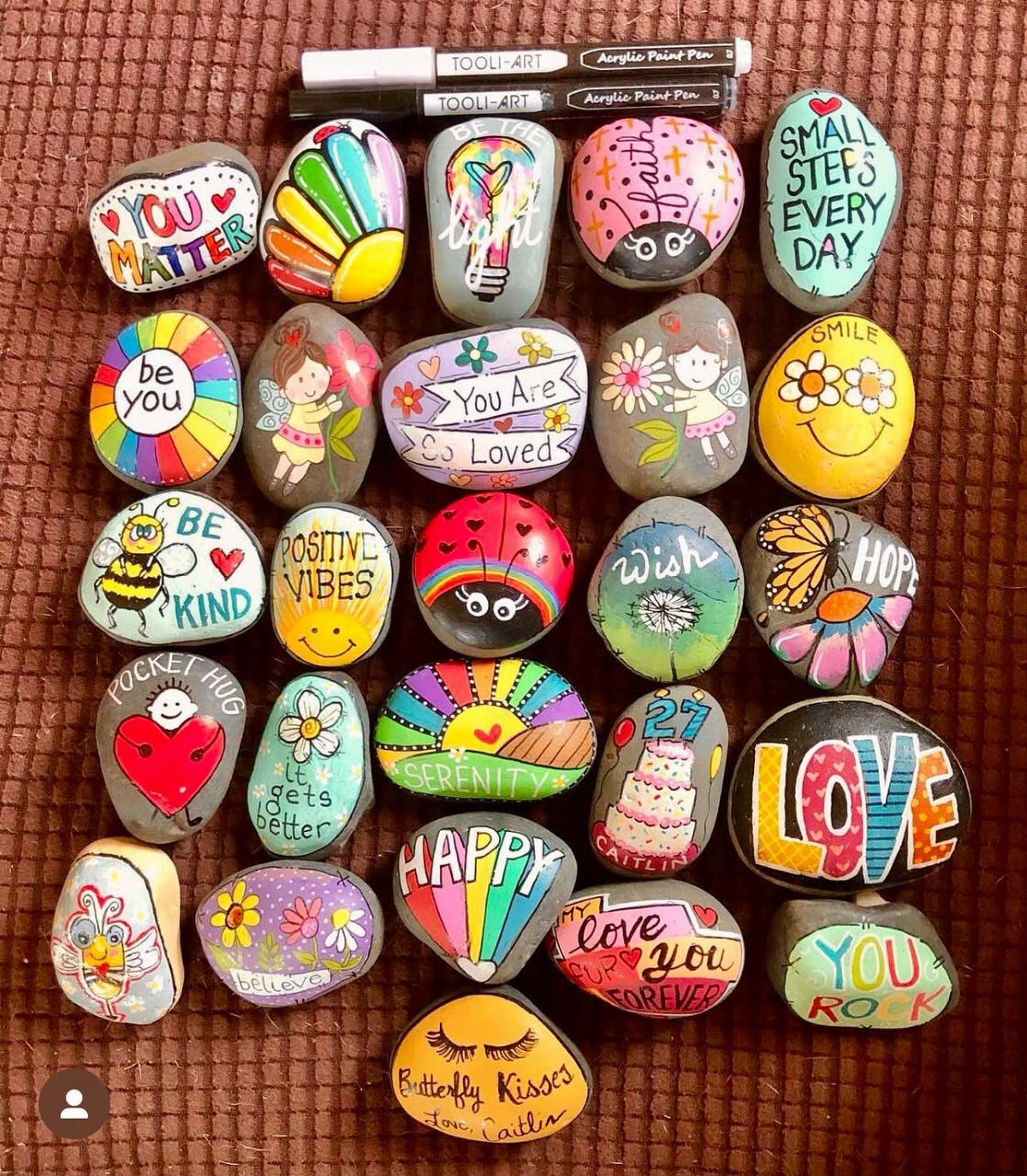 Colorful painted rocks with inspirational words and patterns arranged on a brown textured surface.