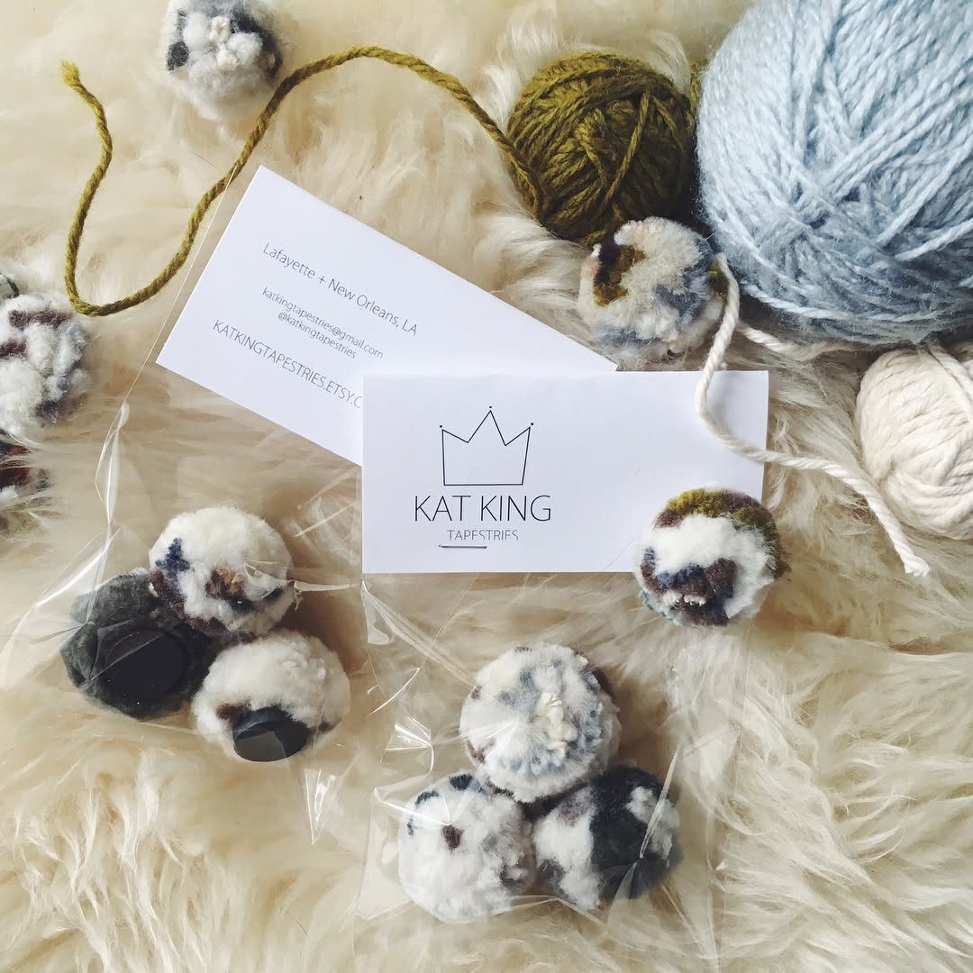 Small multicolored pom poms scattered on white faux fur near a business card.