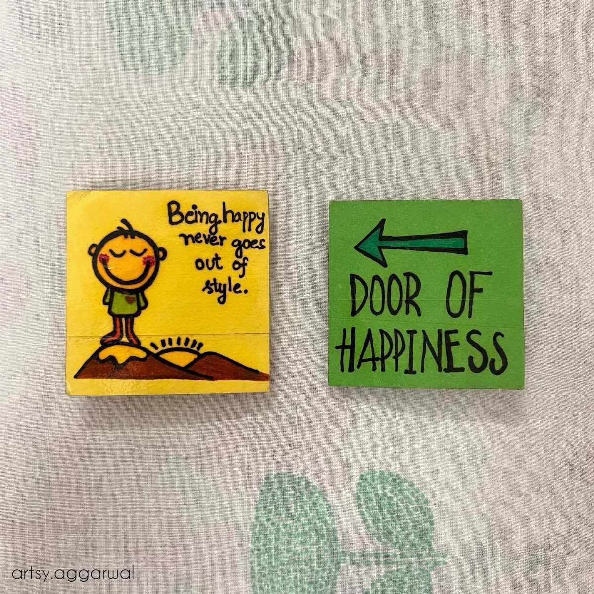 Two hand-painted wooden square magnets with inspirational quotes and colorful illustrations on a light background.