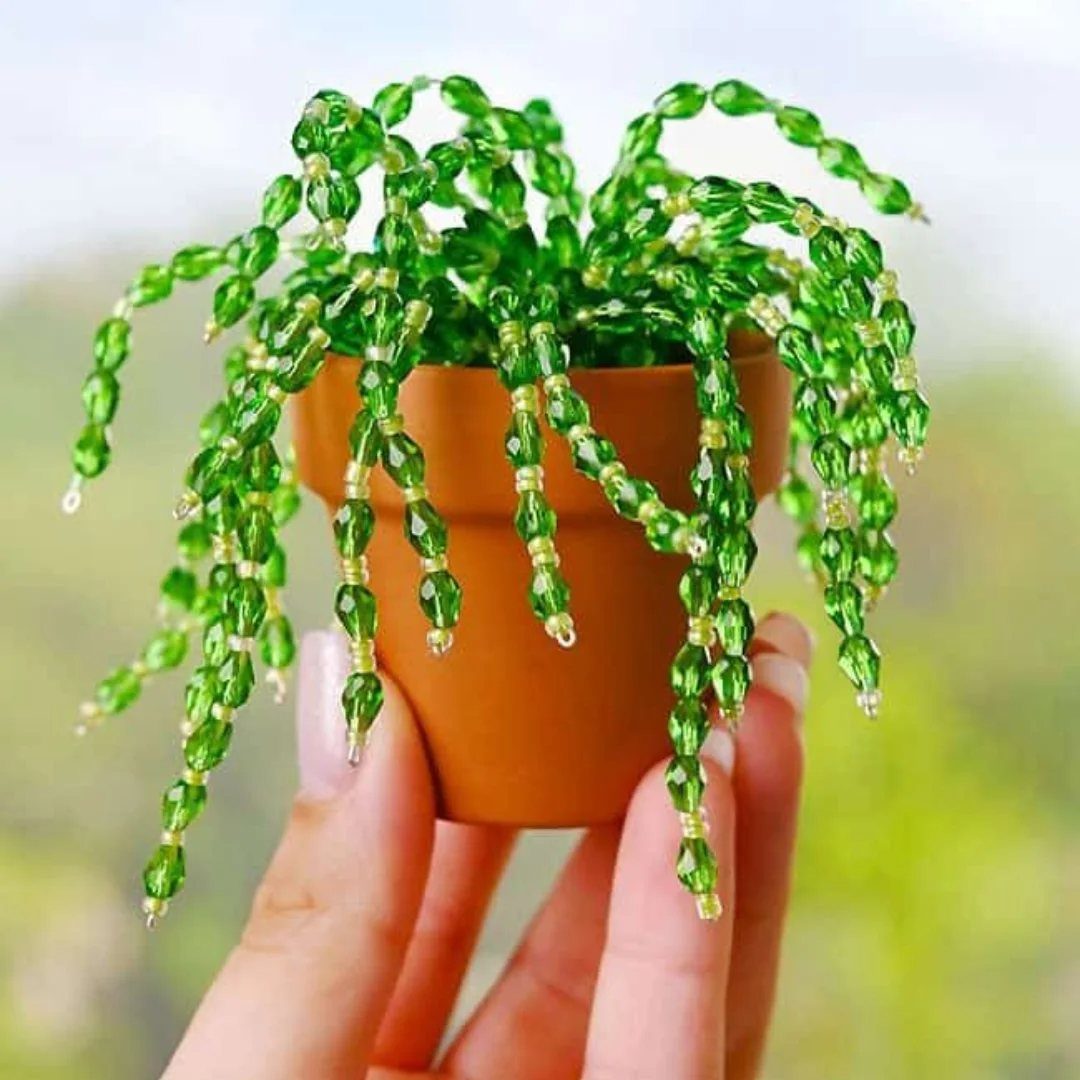 A hand holding a miniature terracotta pot filled with a cascading green bead plant.