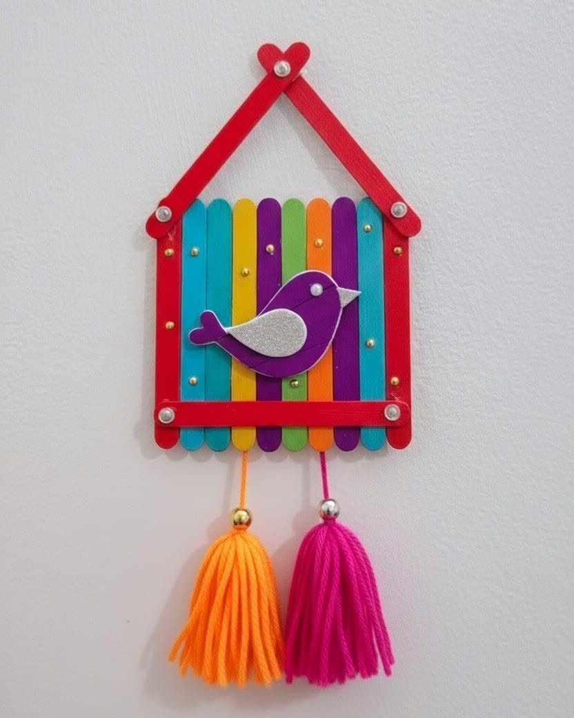 Colorful ice cream stick craft shaped like a house with a bird and yarn tassels.
