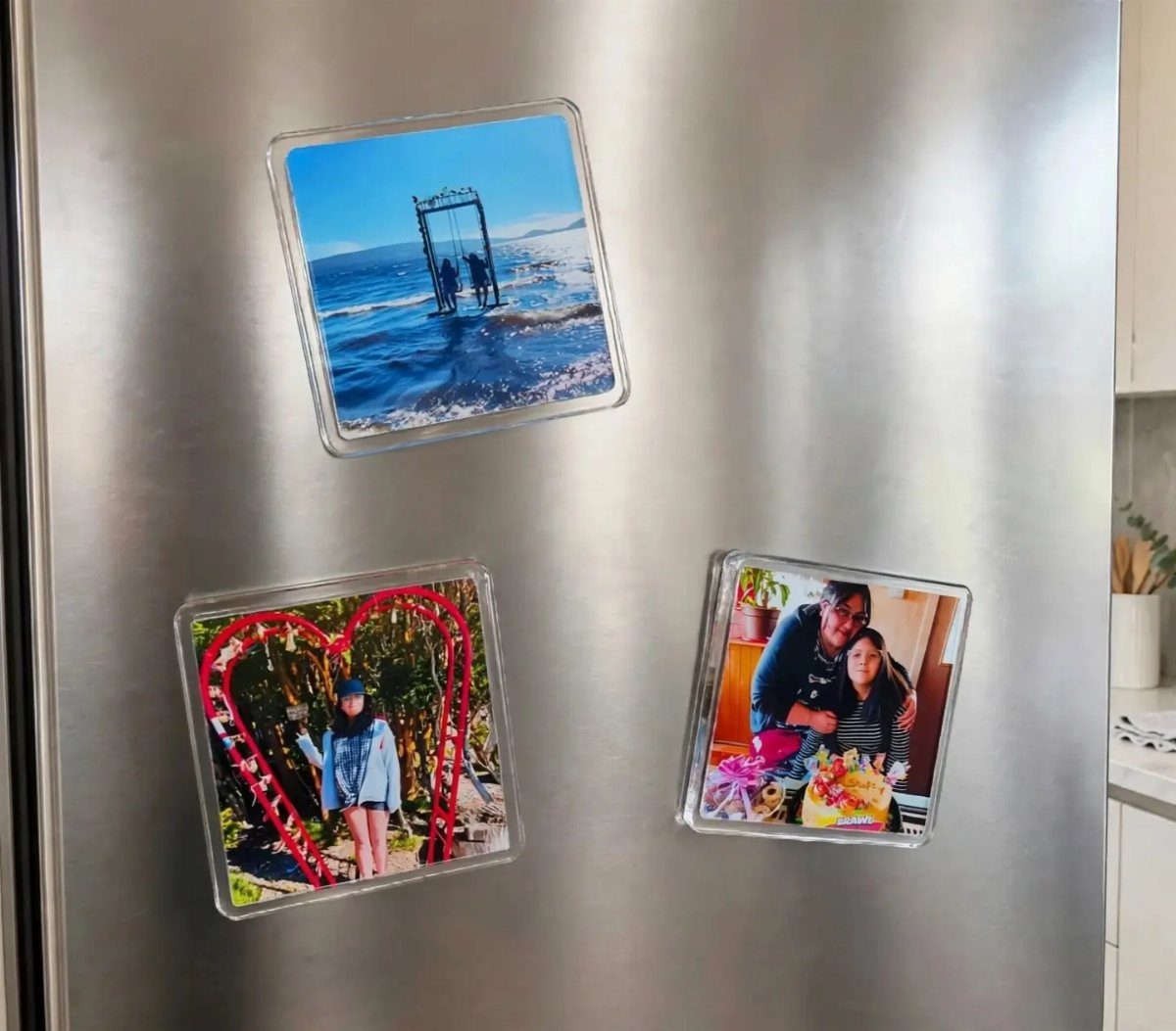 Three square photo magnets displaying various personal memories attached to a silver refrigerator.
