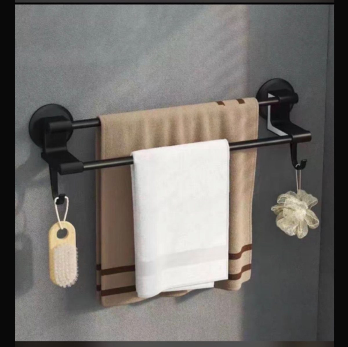 Black towel bar with hanging towels, a wooden brush, and a bath sponge on a grey wall.