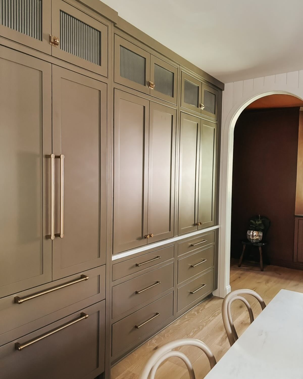 Taupe built-in kitchen cabinetry with gold handles concealing integrated appliances and a refrigerator.