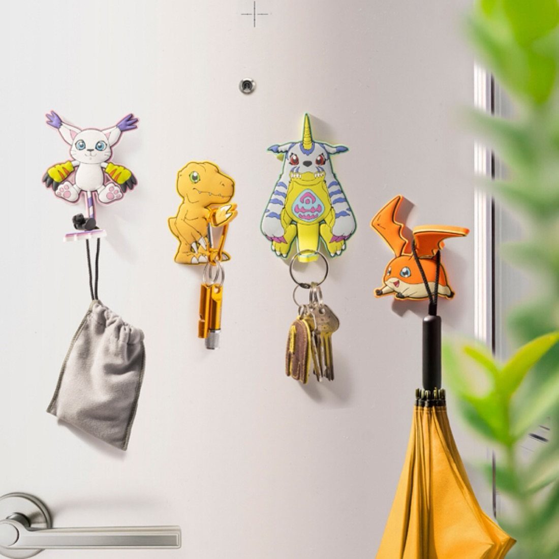 Cartoon character magnets hanging a grey pouch, keys, and a yellow umbrella on a white door.