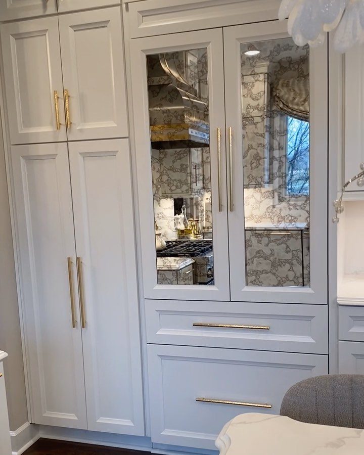 Light gray kitchen cabinets with mirrored refrigerator door panels and gold hardware.