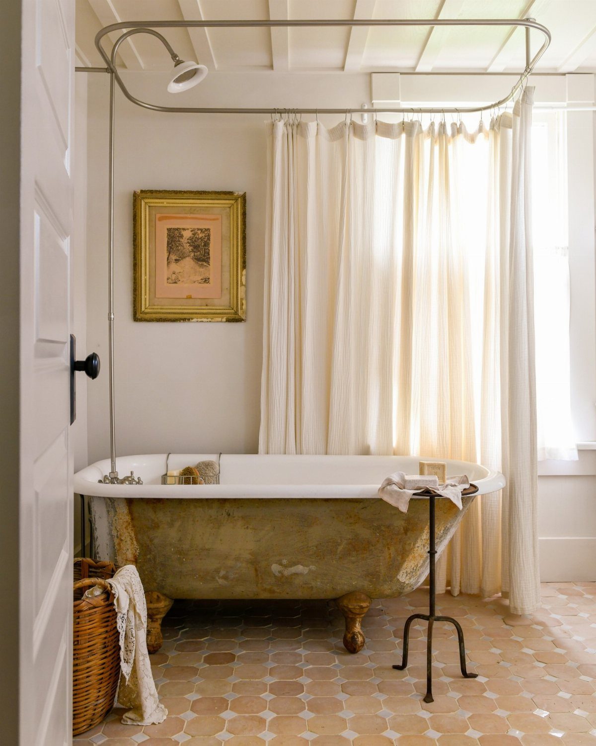 A weathered gold clawfoot bathtub positioned against a white curtain and tiled floor.
