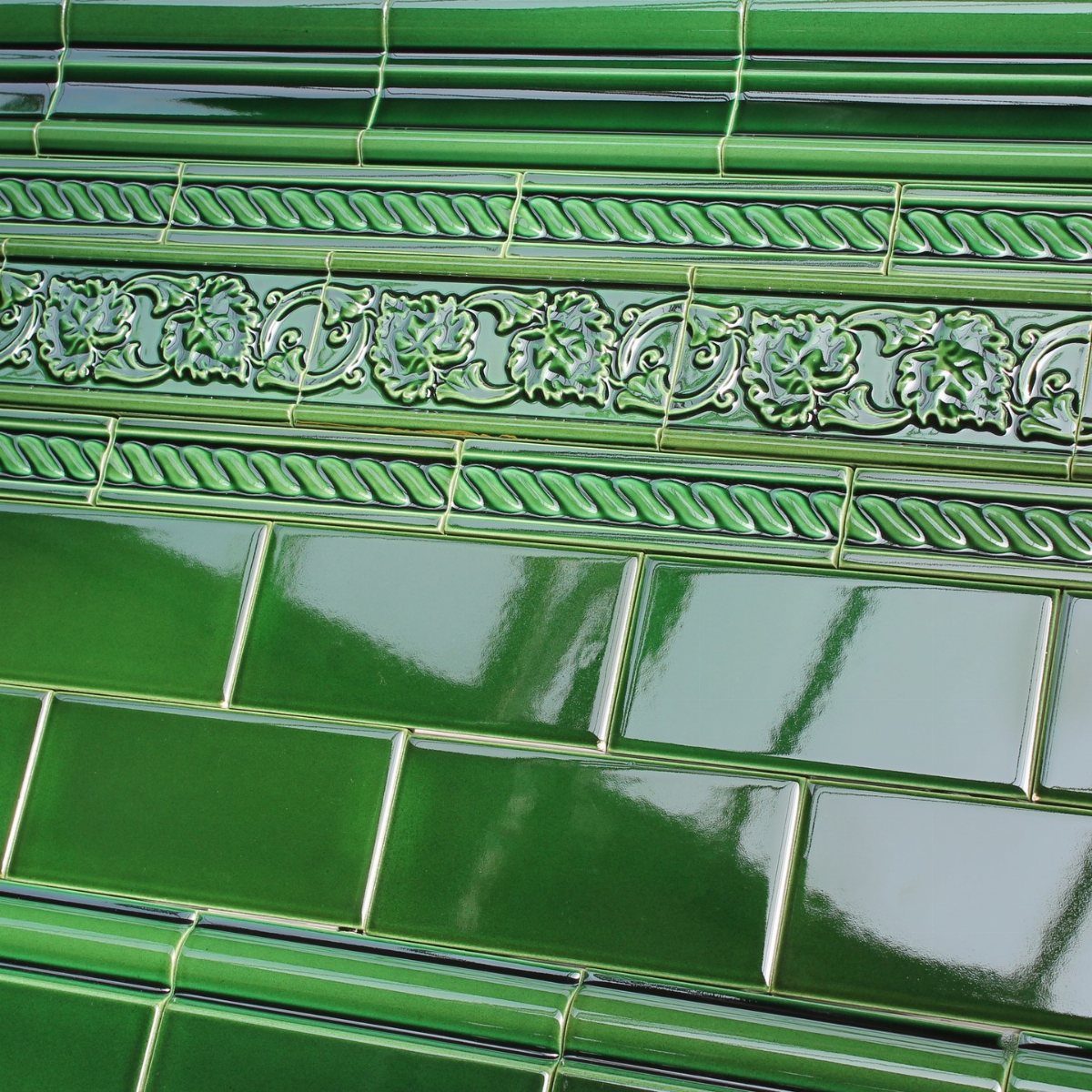Glossy green subway tiles with decorative leaf and rope pattern borders.