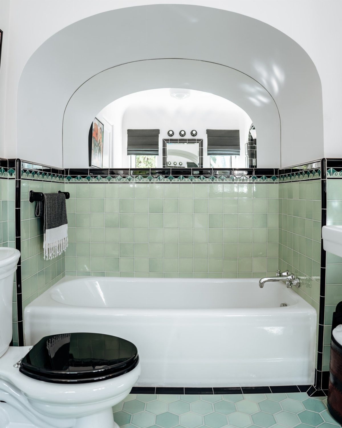 White bathtub and toilet set against light green square wall tiles and blue hexagon floor tiles.