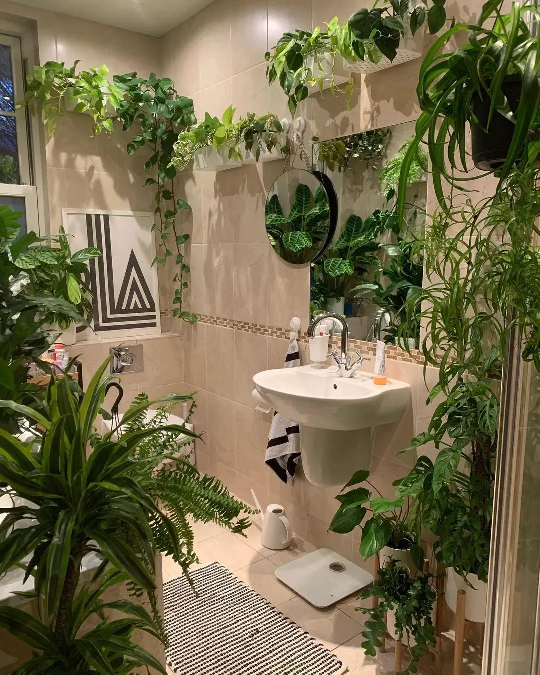 Lush green plants in various containers surrounding a white pedestal sink in a tiled bathroom.