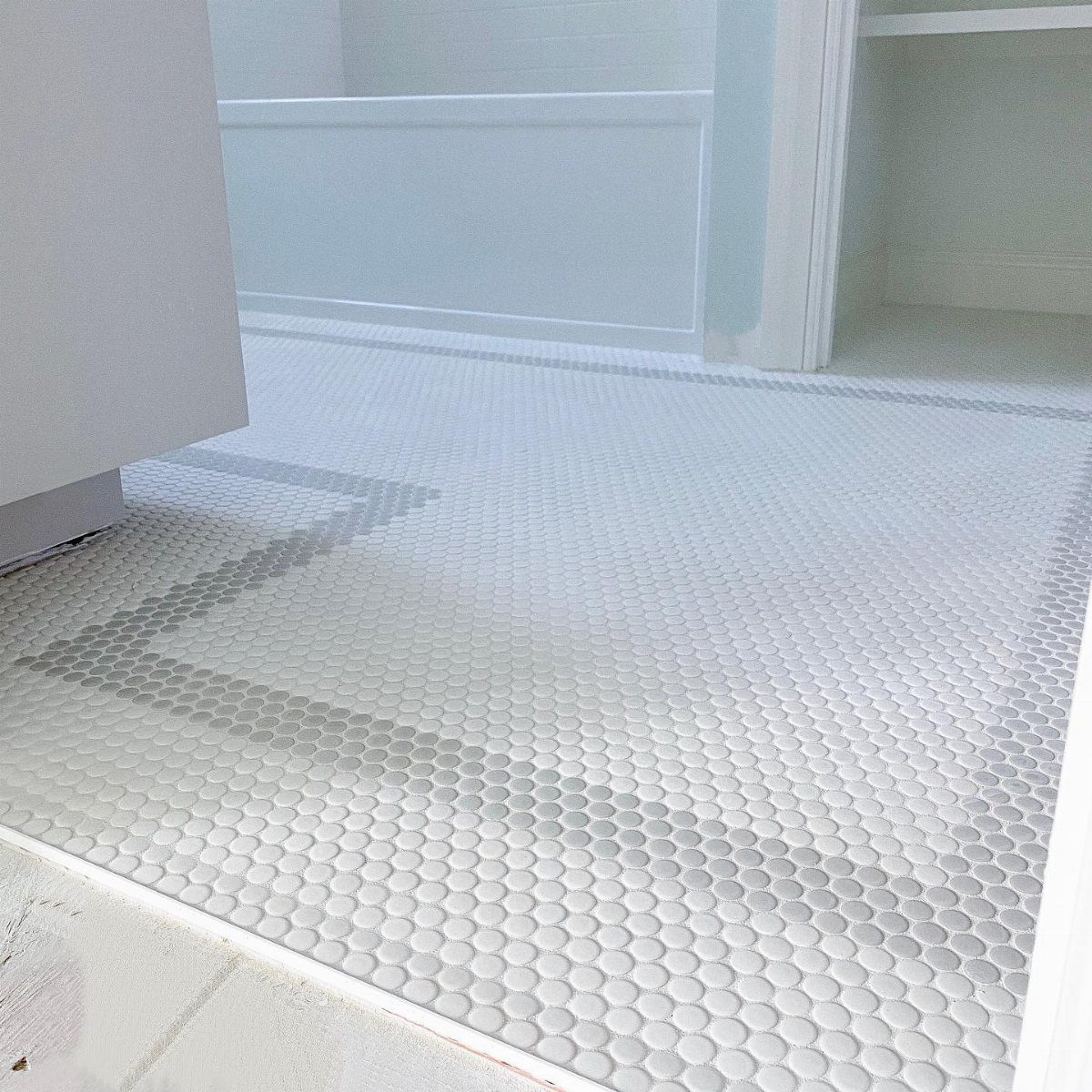 White penny tiles with a light grey geometric border pattern on a bathroom floor.