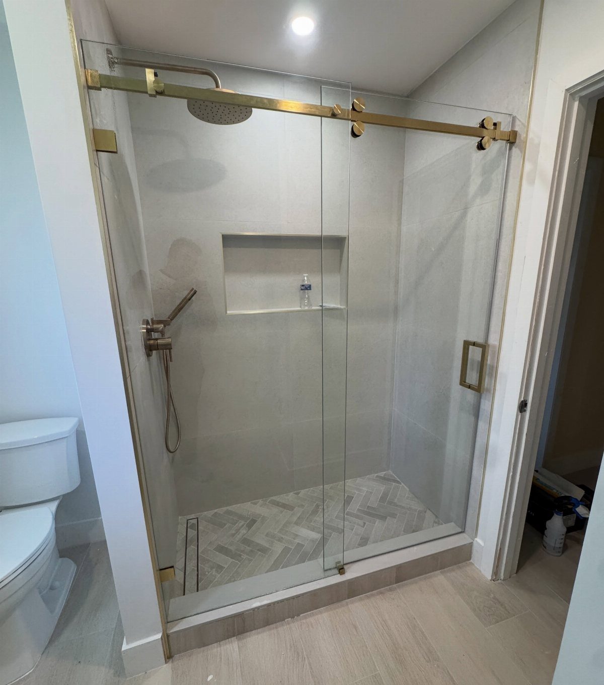 Gold hardware and fixtures on a modern glass walk-in shower with grey tiling.