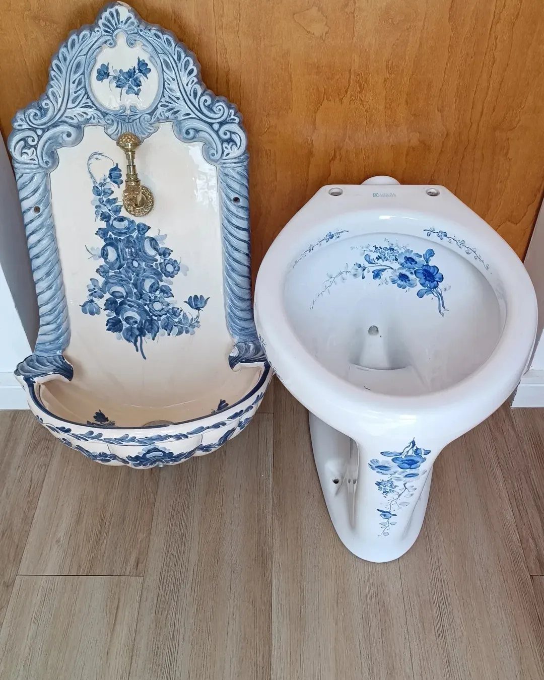 Blue floral patterned ceramic bidet and wall-mounted sink against a wooden wall.