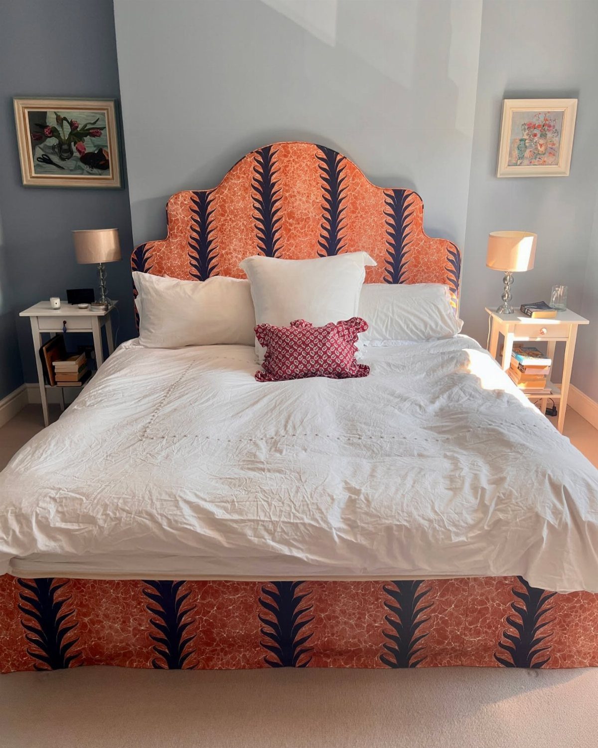A bed with a large orange and navy blue patterned scalloped headboard and white bedding.