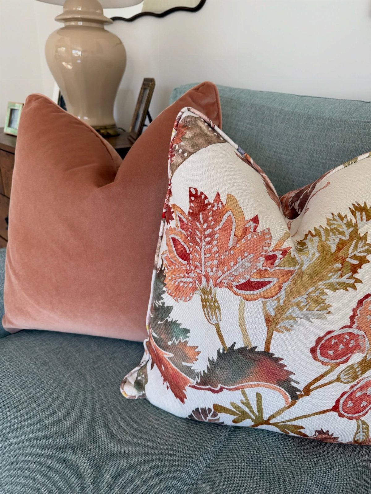 Two decorative pillows, one solid rose velvet and one floral patterned, resting on a teal sofa.